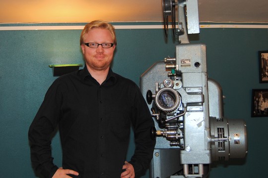 Kinosjef Ole Johan Grøndal Hansen ønsker i kveld velkommen til digital kino på Festiviteten. Her foran den nostalgiske kinomaskinen i foajéen. [i](Arkivfoto: Adrian Sellstrøm)[/i]